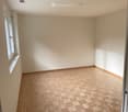 Empty room with white walls, wooden floor, small window.