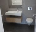 Bathroom with white sink, mirror, modern toilet, gray walls and floor.