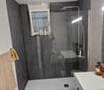 Bathroom with shower, sink, toilet, grey walls, clear glass door, white floor, towels hanging on the wall.