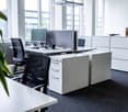 Open office layout, desk, chairs, computer monitor, shelves, plants, white color scheme, window
