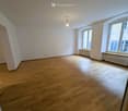 Empty room with white walls, wooden floor, radiators, windows with view of the outside
