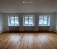 Empty room with wooden floor, three large windows, white walls, and white radiators under the windows