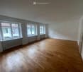 an empty room with hardwood floors, white walls, windows with radiators