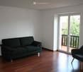 Two piece sofa, armchair, sliding door to balcony, white walls, wooden floor