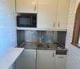 compact kitchen with white cabinets, sink, oven, and microwave, tiled floor