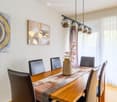 wooden dining table, black chairs, dining lamp, artwork on the wall, white curtains
