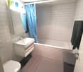Bathroom: white tiles, sink, bathtub, toilet, mirror, towel rack, towel