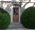 front view of stone house with wooden door, hedges