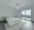 large white bed, white bedside tables, large sliding glass doors to balcony, round ceiling chandelier