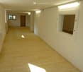 Empty room, white brick walls, wooden floor, windows, and doors at the end.