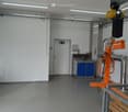 Empty room, white walls, gray floor, small kitchen area, sink, and blue cabinet, orange machinery, pipes and electrical wiring