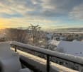 snow-covered balcony with chairs, snowy roofs of houses, a tree, a view of mountains and sky