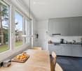large windows with view of outside, wooden table, wooden chairs, kitchen counter, kitchen appliances