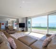 Modern living room with glass sliding doors, L-shaped sofa, carpet, TV, view of a grassy terrace and the sea