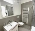 modern bathroom with a white sink, glass shower cabin, toilet, radiator, mirror, and washing machine