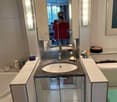 Bathroom with a sink, mirror, bathtub, and toilet, modern design, vanity with cabinets, tiled walls and floor, and mounted lamps.