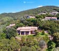 Villa in a hilly landscape, tiled roofs, surrounded by trees, with a clear sky above.