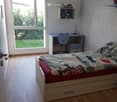 wooden floor, white brick wall, glass door, desk, blue chair, lamp, bed with drawer