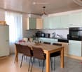 wooden table with 6 brown chairs, kitchen area with oven, dishwasher, wooden ceiling