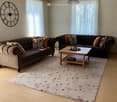 Two brown sofas, wooden coffee table, large rug, white drapes, wall clock, wooden floor