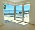 modern interior, large glass sliding doors, wooden flooring, balcony overlooking the sea, scenic mountains in the distance