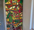 A room entrance with a large stained glass wall depicting geometric patterns with various colors including red, green, yellow, and brown.