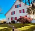 2-story white house with red shutters, brick pathway, grassy lawn, tree, outdoor lamp, bright blue sky