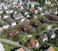 Aerial view of a residential area with various buildings, a garden in the center, and some buildings with green roofs and solar panels