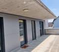 Modern balcony with tiled floor, large glass sliding doors, wooden ceiling, and built-in lighting.