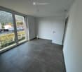 Empty room with grey tiled floor, white walls, large sliding glass door leading to outdoor view, and a closed white door.