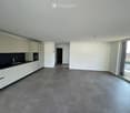 Empty kitchen with white cabinets, black countertop, and large windows, connected to a hallway.