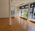 an empty room with parquet flooring, two pillars in the center, large windows on the right, two benches under the windows, a ceiling lamp