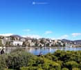 A lake with a view of a city with many buildings, mountains, trees, and people on a clear day