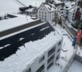 White building with balconies, solar panels on the roof covered in snow, surrounded by snow-covered landscape