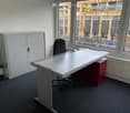 white desk, black chair, white cabinet, red storage box, gray carpet, window with view of city