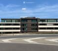 Modern three-story building with large windows and a flat roof, situated near a road with clear markings.