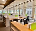 Modern office space with multiple desks, chairs, and cabinets arranged in rows, large windows with blinds, and a clean, organized layout.