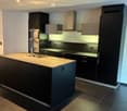Modern kitchen with dark cabinets, granite countertop, stainless steel appliances, and integrated lighting.