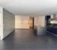 Modern kitchen with dark tiled floor, grey brick accent wall, kitchen island with sink, and dark cabinets.