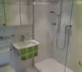 Modern bathroom with white tiles, a glass-enclosed shower, a toilet, a sink with a green towel, and a mirror cabinet.