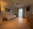 A furnished room with a bed, a small table, chairs, a mirror, a floor lamp, curtains, a radiator, and a television.