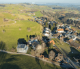 Aerial view of a village with multiple buildings, green fields, and trees.