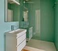 Bathroom with white fixtures, teal tiled walls, glass shower, white vanity, modern design.
