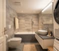 Modern bathroom with a bathtub, toilet, sink, and mirror. Features a wicker basket and a towel on the floor.