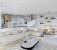 Modern L-shaped living room with couch, table, round staircase, kitchen, dining table, and a white color scheme.