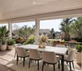 Balcony / Terrace. Balcony with a modern dining setup, including a white table, six chairs, a vase with dried flowers, and several potted plants. The balcony has a view of a suburban neighborhood with houses and trees.