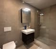 Modern bathroom with a white toilet, a sink with a dark wooden cabinet, a mirror with built-in lighting, and a glass-enclosed shower area.