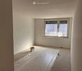 An empty room with white walls, a large window, and a white sheet covering the floor.