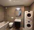 Modern bathroom with a bathtub, toilet, sink, mirror, and stacked washing machine/dryer unit.