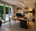 Furnished Room. A desk with a computer monitor, keyboard, and mouse. A lamp and a plant are on the desk. A chair is placed in front of the desk. A picture frame and a book are on the shelf. A potted plant is on the floor. A lamp is on the right side. A ru
